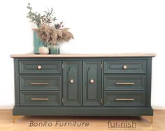 the sideboard is painted green and has gold hardware on it's drawers, along with a potted plant