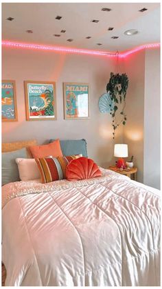 a bedroom with pink lights and pictures on the wall above the bed, along with an orange throw pillow