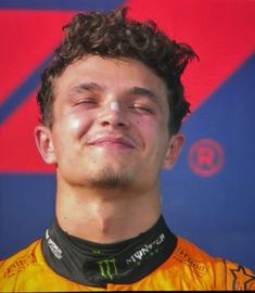 a close up of a person with curly hair and wearing a yellow shirt smiling at the camera