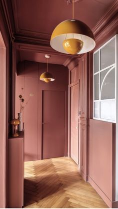 an empty hallway with pink walls and wooden floors, two lamps hanging from the ceiling