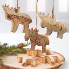 three wooden moose ornaments hanging from chains on a piece of wood with pine branches in the background