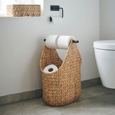 a bathroom with a toilet and wicker basket on the floor, next to a roll of toilet paper