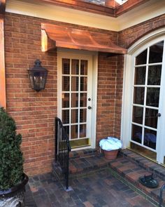 a brick house with two doors and a glass door on the front porch, surrounded by potted plants