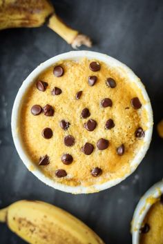 a bowl filled with chocolate chips next to some ripe banana's on a table