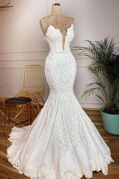 a white wedding dress on display in front of a potted plant