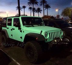 a green jeep parked in a parking lot next to palm trees at night with the sun setting