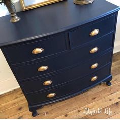 a black dresser with gold handles and knobs next to a framed photo on the wall