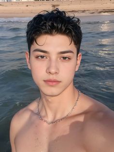 a shirtless young man standing in the water wearing a silver chain around his neck