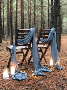 two wooden chairs sitting in the middle of a forest with blue blankets draped over them