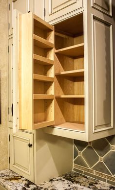 an open cabinet in the middle of a kitchen countertop with marble counters and white cabinets