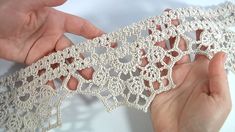 two hands are holding a piece of white lace