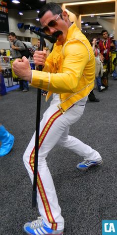 a man in yellow jacket and white pants holding a black pole while standing on carpet