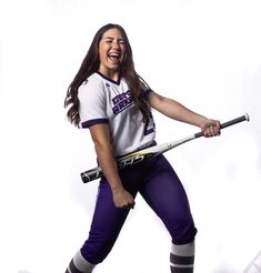 a woman in purple and white uniform holding a baseball bat with her right arm out