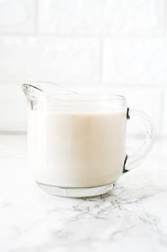 a glass pitcher filled with milk sitting on top of a marble countertop next to a white tile wall