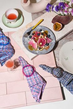 a table topped with plates and cups filled with food next to teapots on top of a pink tiled floor