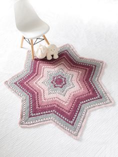 a crocheted star rug on a bed with a white chair and teddy bear