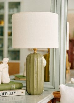 a green lamp sitting on top of a table next to a book and a mirror