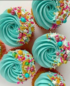 four cupcakes with blue frosting and sprinkles on white background