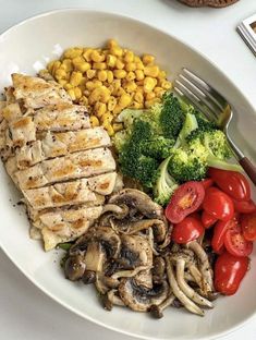 a white plate topped with meat, veggies and corn next to a fork