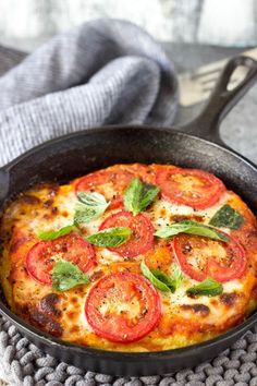 a pizza with tomatoes and basil in a cast iron skillet on a gray towel