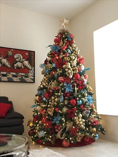 a decorated christmas tree in a living room with red, blue and gold ornaments on it