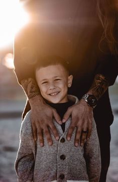 a young boy smiles as he holds his mother's arm in front of the sun