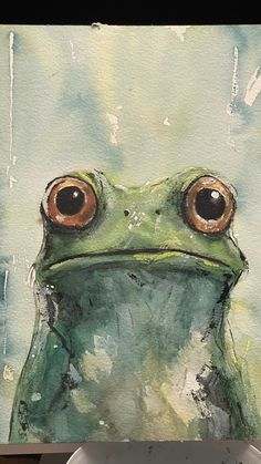 a painting of a green frog with big brown eyes on a white plate next to a cup