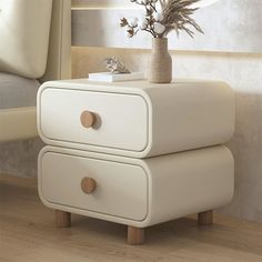 a white table with two drawers and a vase on top of it next to a bed