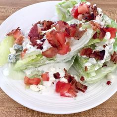 lettuce with bacon, tomatoes and blue cheese on it sitting on a white plate