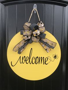 a welcome sign hanging on the front door of a house with a bee and checkered bow