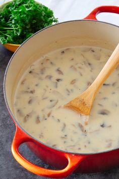 a red pot filled with mushroom soup next to a green leafy vegetable on the side