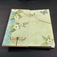 an open book with white flowers and green leaves on the cover is sitting on a black surface