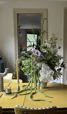 a vase with flowers sitting on top of a table next to a candle and some chairs