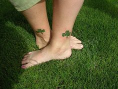 two people with tattoos on their feet standing in the grass