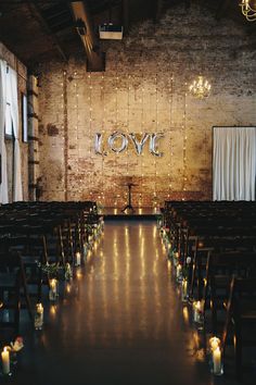 an aisle lined with candles in front of a brick wall and decorated with love sign