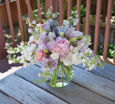 a glass vase filled with lots of flowers on top of a wooden table next to a fence