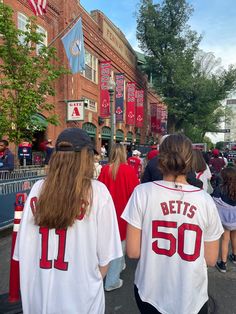 two women in baseball jerseys walking down the street with people watching them from their seats