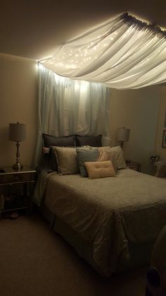 a bed sitting under a canopy in a bedroom next to a night stand with lights on it