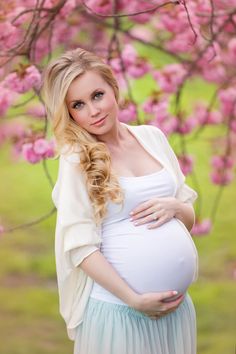 a pregnant woman standing in front of a tree with pink flowers