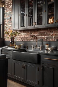 a kitchen with black cabinets and wooden floors, brick wall behind the sink is an old fashioned faucet