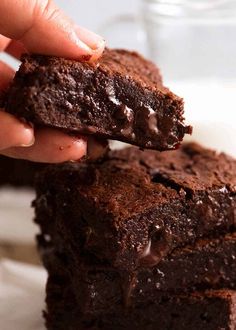 a person holding a chocolate brownie in their left hand and the other one has it's bite taken out