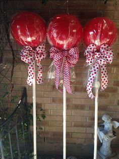 three red balloons tied to white sticks with bows on them in front of a brick wall