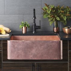 a copper sink in a kitchen with black counter tops and wooden cabinets, surrounded by potted plants