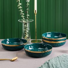 three green bowls with gold rims on a table next to a candle and vase