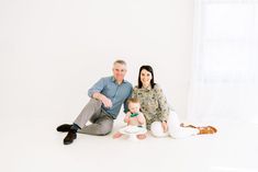 a man, woman and baby sitting on the floor in front of a white wall