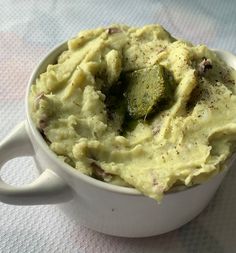 a white bowl filled with mashed potatoes and cucumbers on top of a table