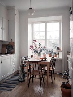 a dining room table and chairs with potted plants in the window sill next to it