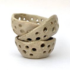 three ceramic bowls with holes in them on a white surface, one is made from clay and the other is handmade