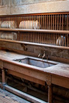 an old kitchen with wooden counter tops and dishes on the shelf above it, in front of a brick wall