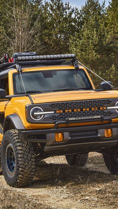 a yellow truck parked on top of a dirt field next to trees and bushes in the woods